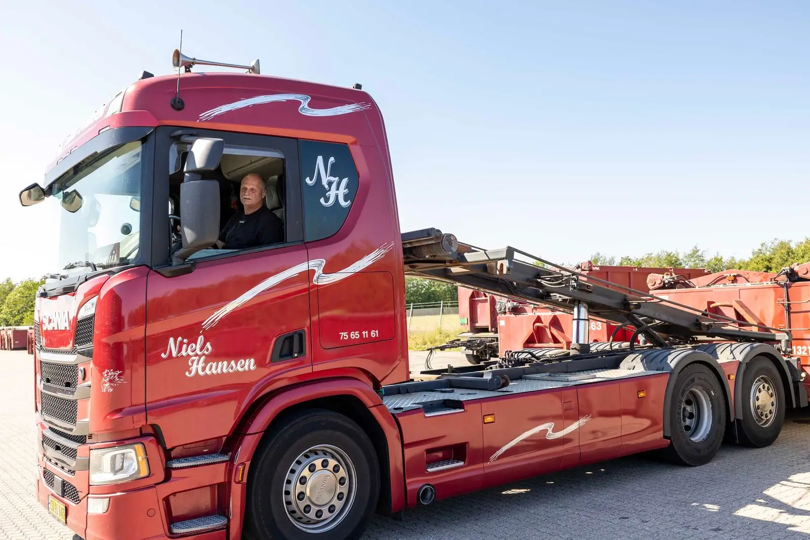 Containerbil med hejset kørt op og åbne affaldscontainere på pladsen
