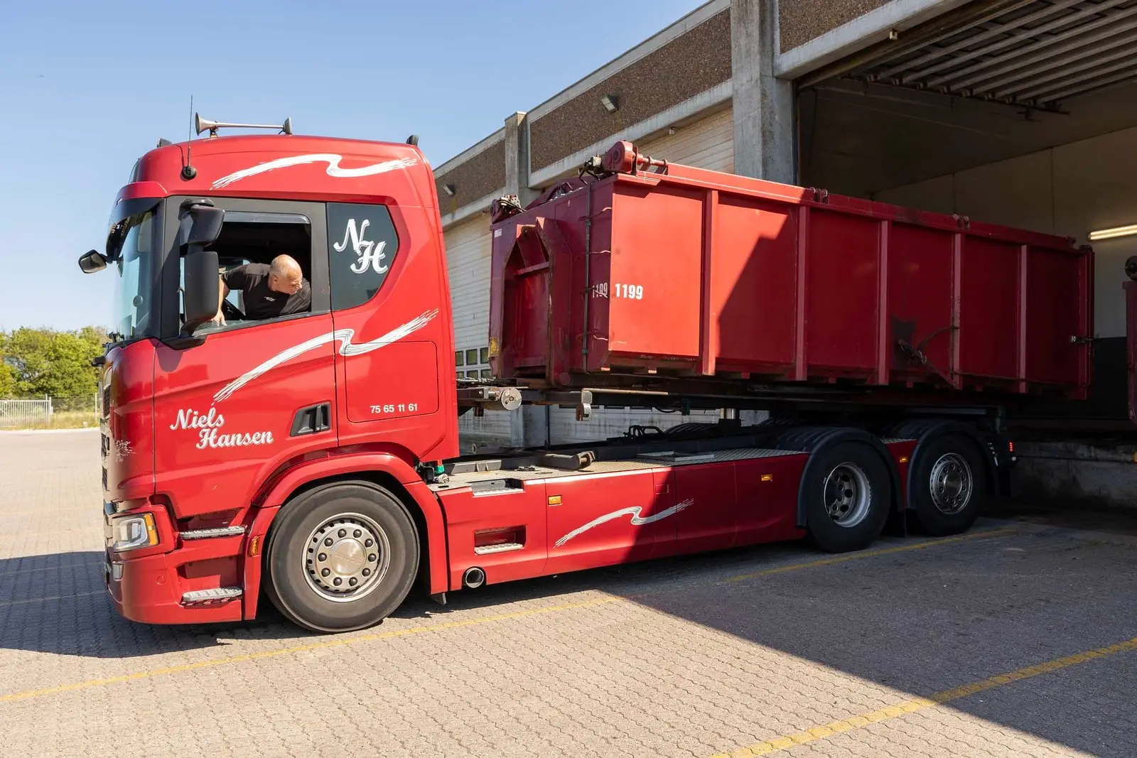 Containerbil i sideprofil med åben affaldscontainer på hejset