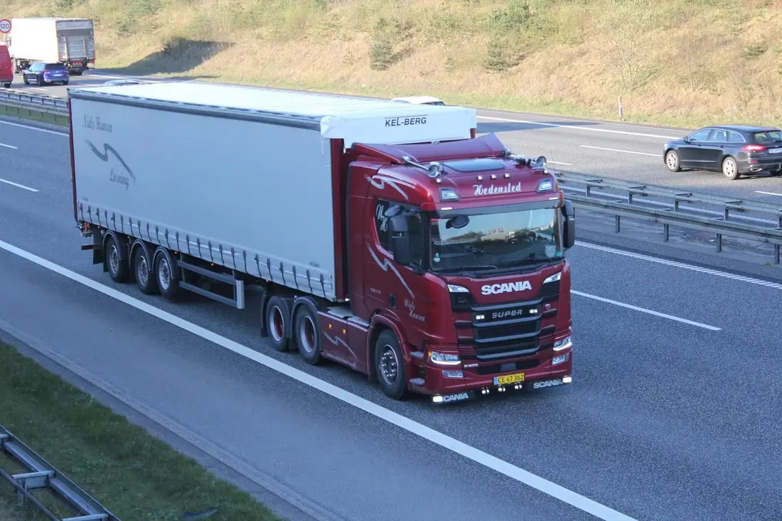 Mørkerød lastbil med hvid gardintrailer på motorvejen set fra en bro