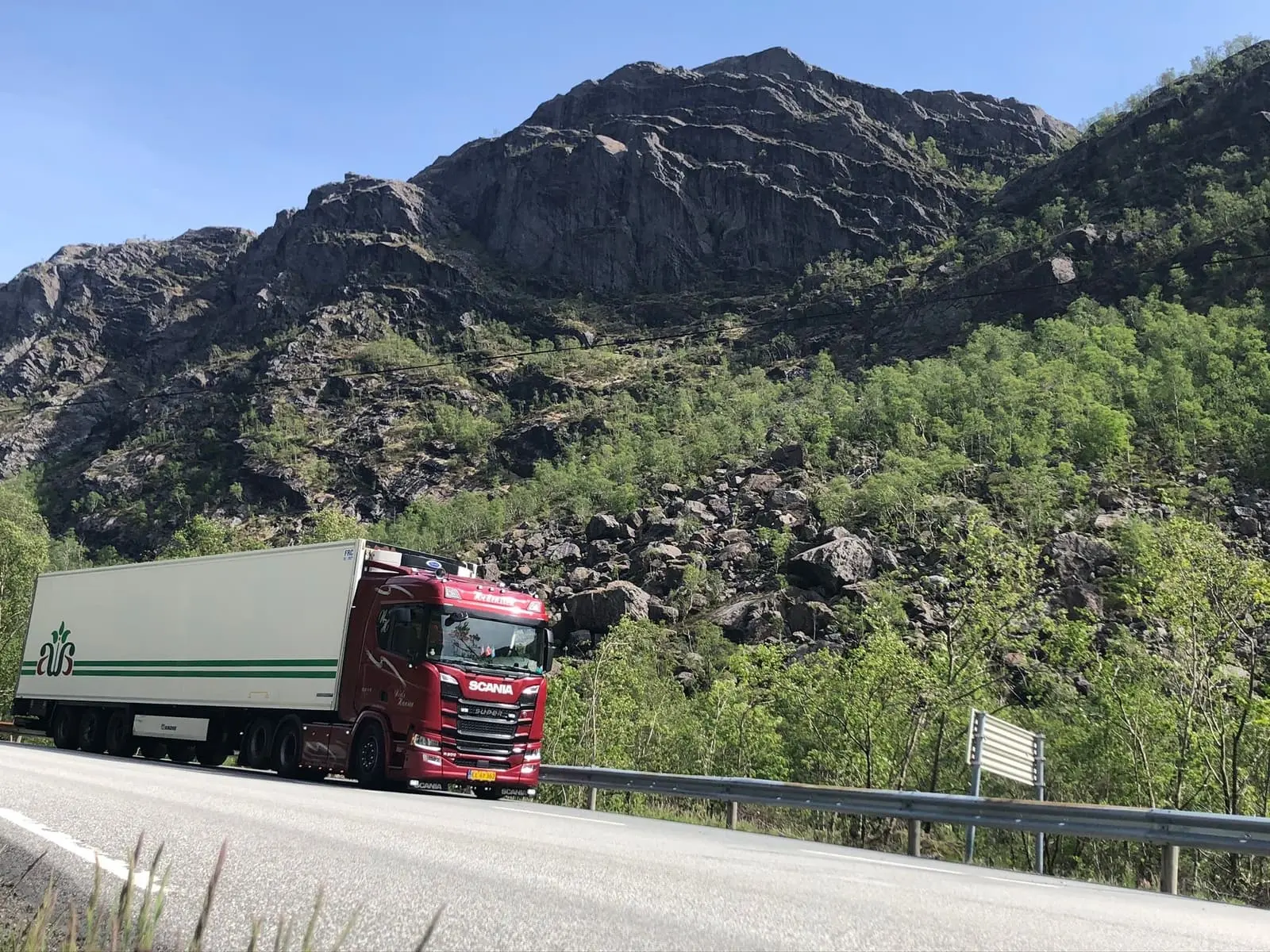 Mørkerød trækker med hvid køletrailer holder i vejsiden under en stejl klippeskråning