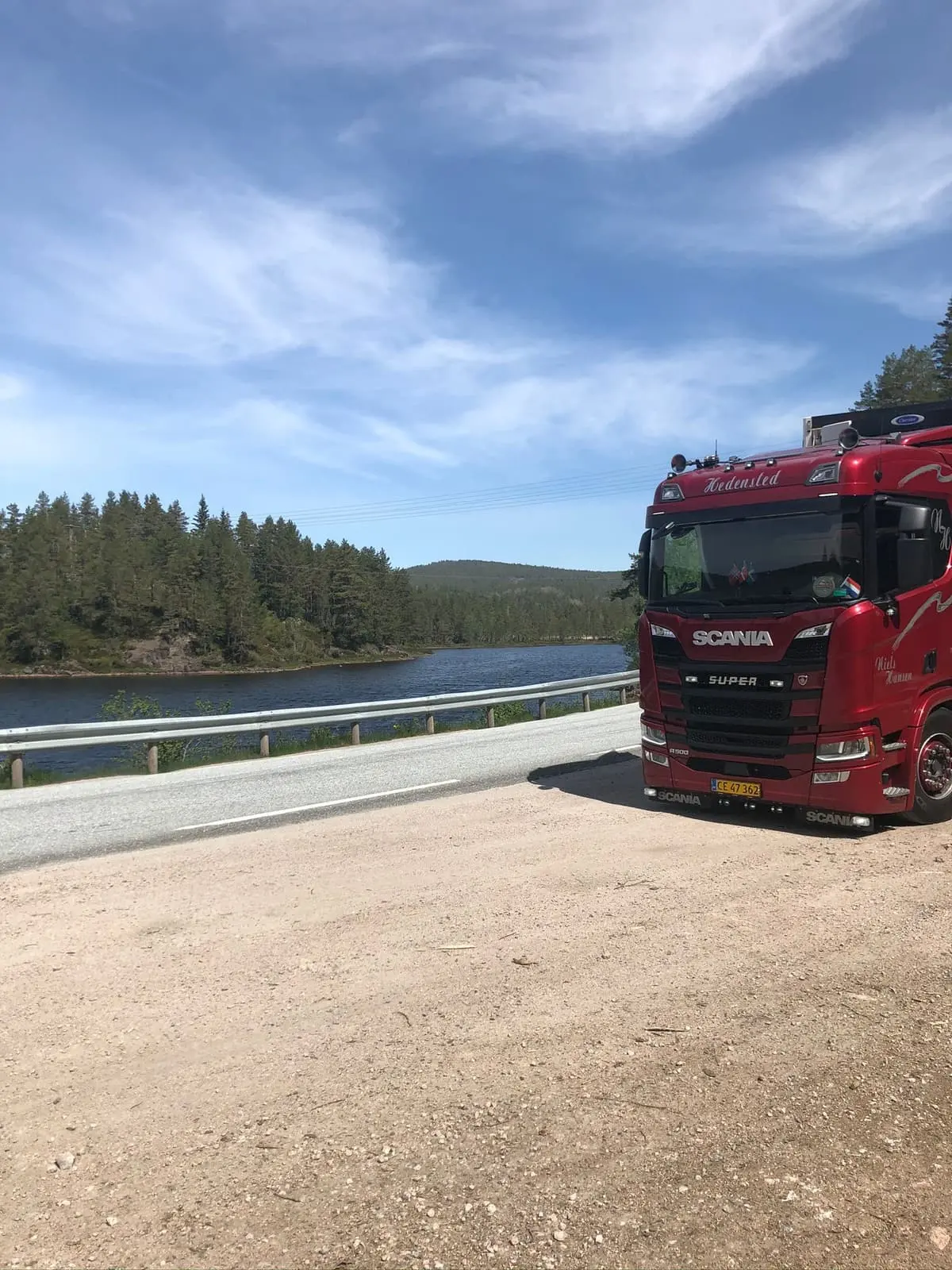 Rød lastbil holder på en grusplads ved vandet