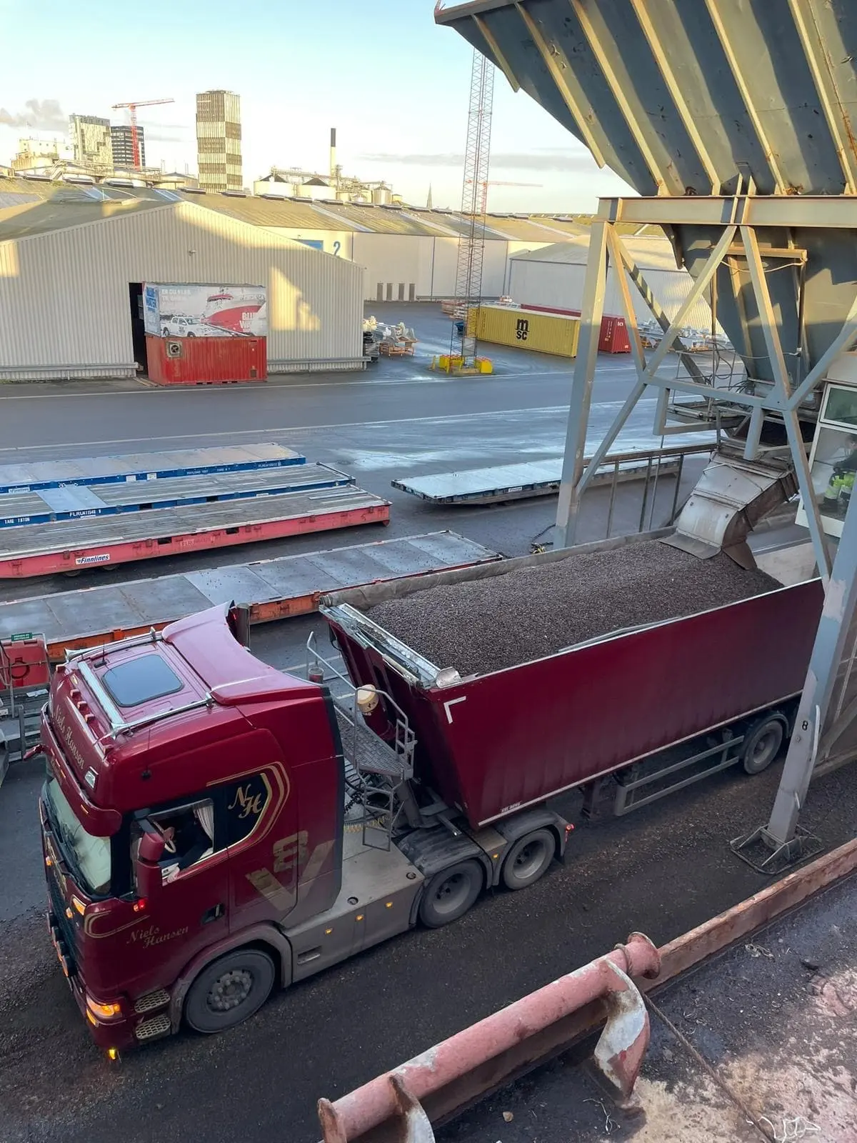 Tippertrailer fyldes med gråt grus fra en stor tragt på havnen