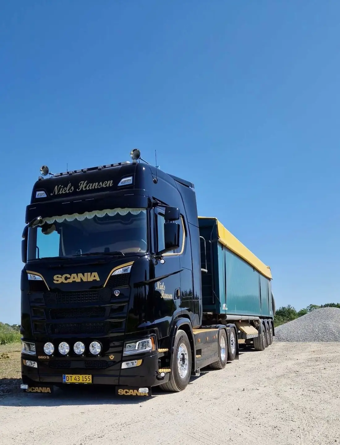 Sort lastbil med guldskrift og grøn tiptrailer på gruspladsen i solskin