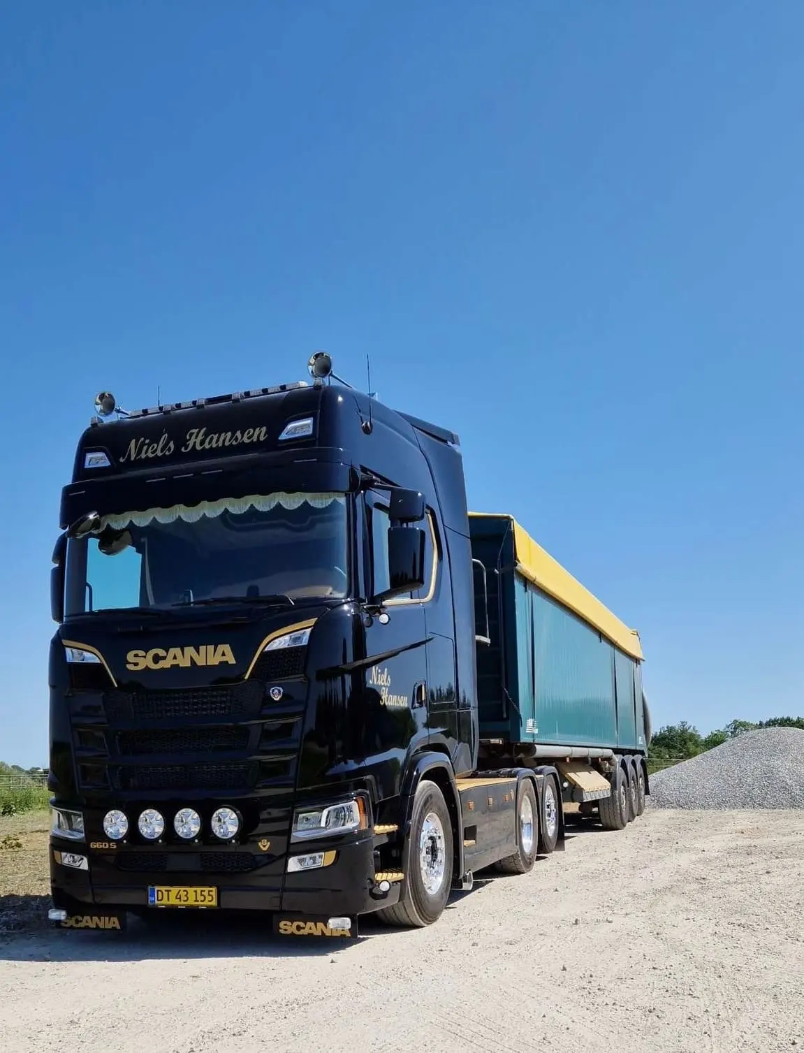 Sort lastbil med guldskrift og grøn tiptrailer på gruspladsen i solskin