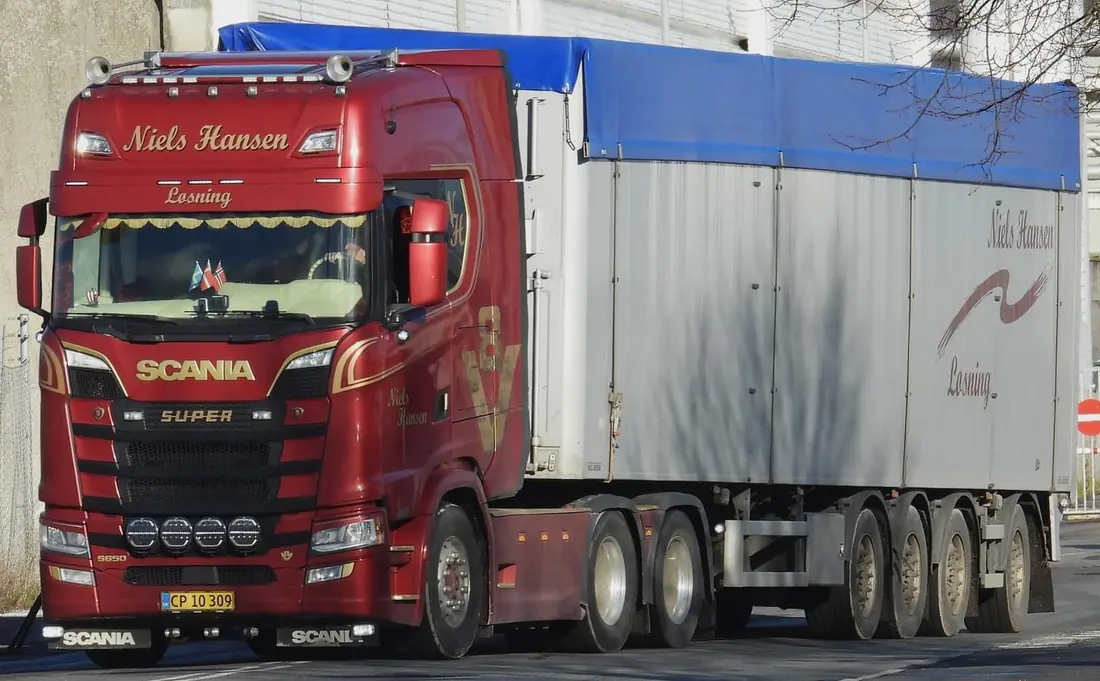 Lastbil med tippertrailer og blå presenning i lavt sollys