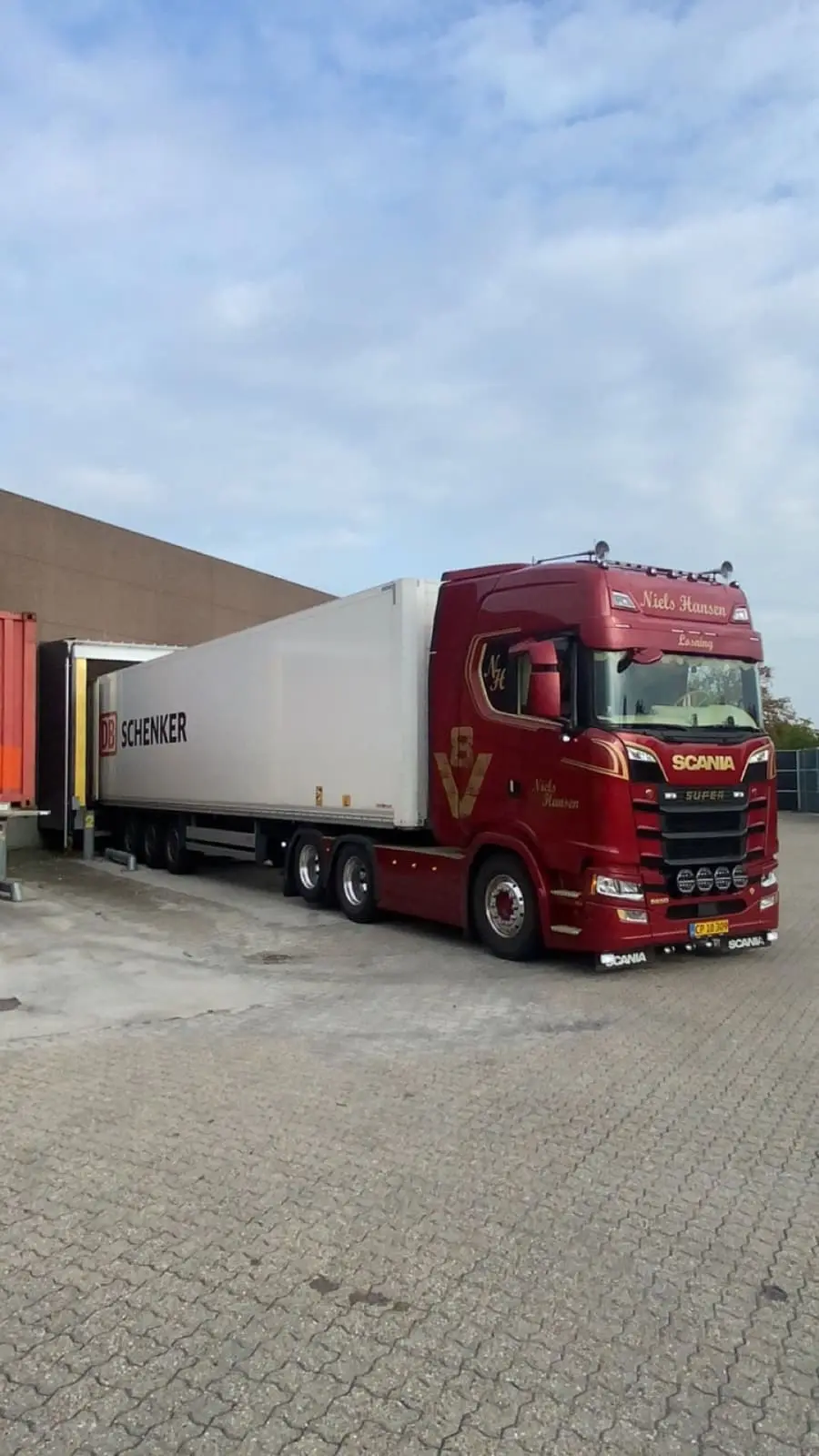 Lastbil med hvid trailer bakket ind til en lagerrampe