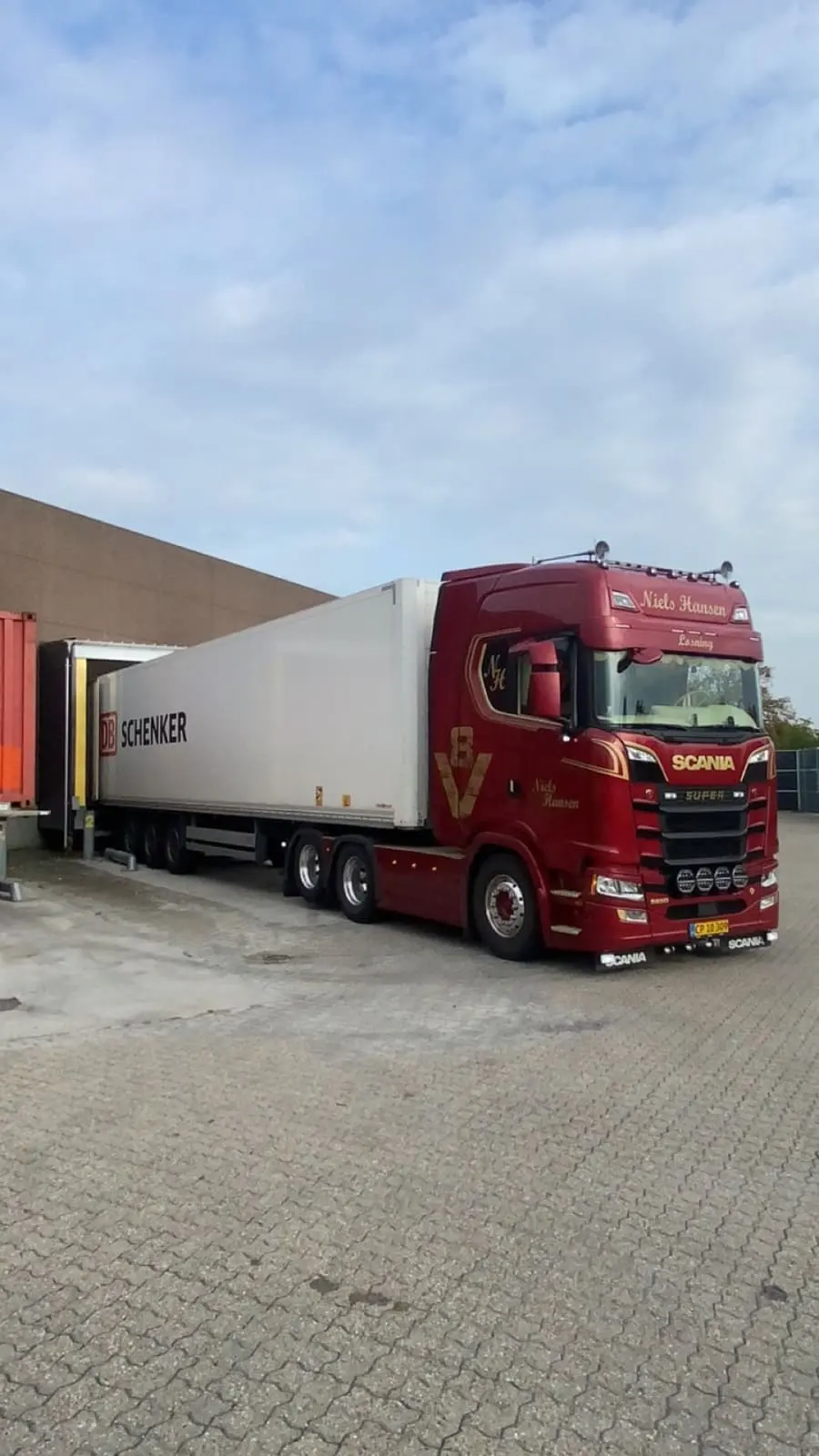 Lastbil med hvid trailer bakket ind til en lagerrampe