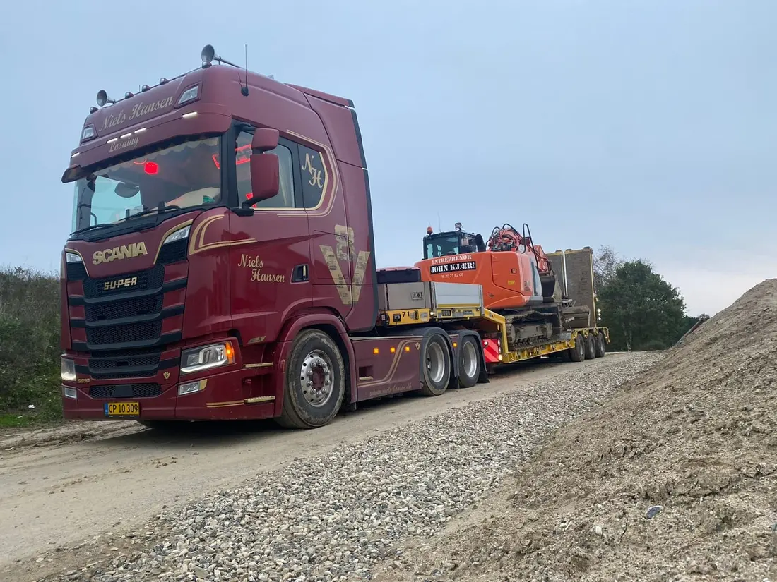 Orange bæltegravemaskine surret fast på maskintraileren på grusvejen