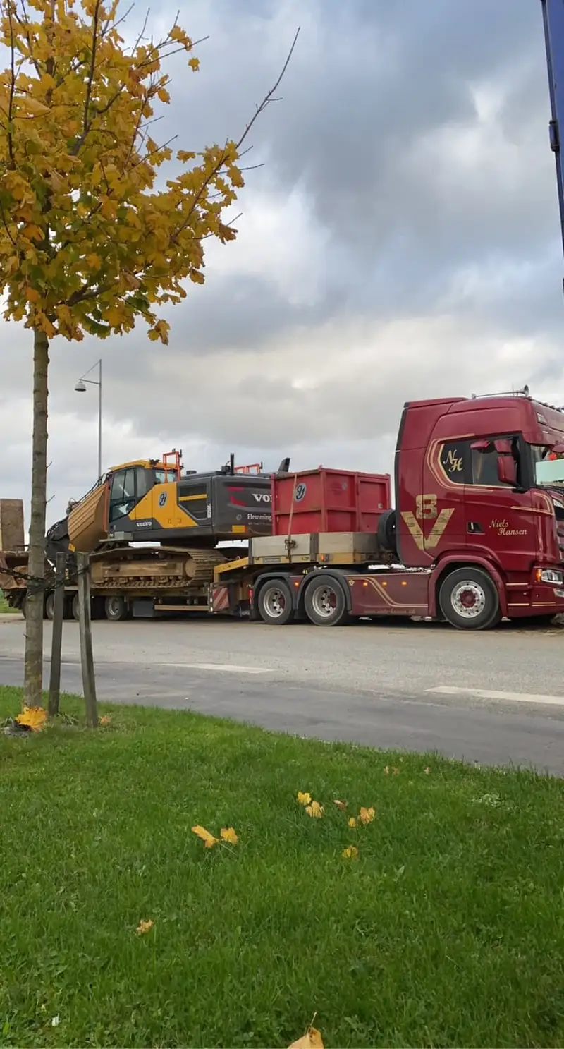 Gul gravemaskine og rød container læsset på maskintraileren bag lastbilen