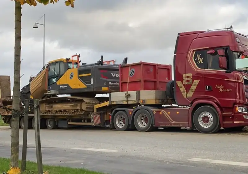Gul gravemaskine og rød container læsset på maskintraileren bag lastbilen