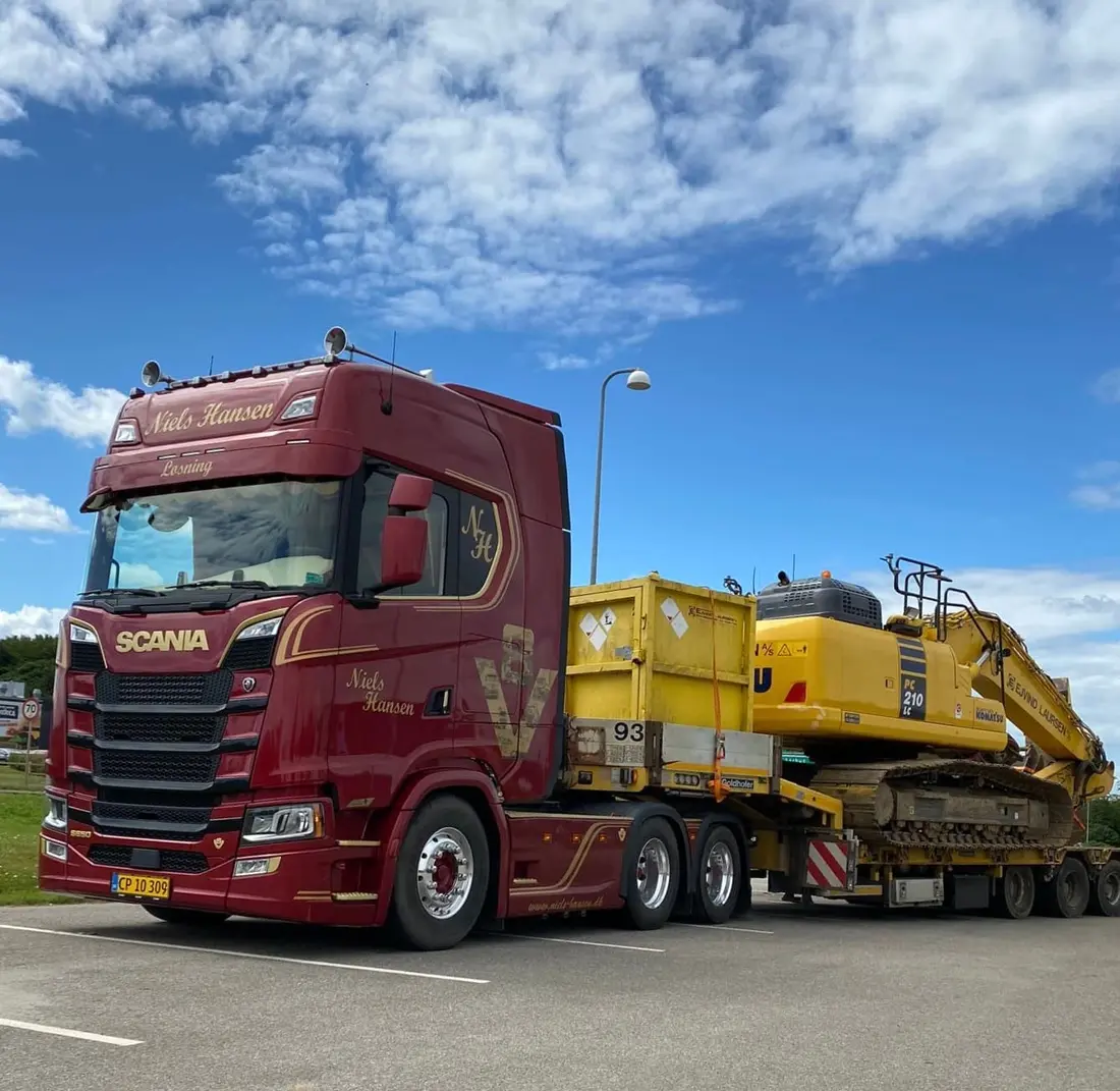 Gul gravemaskine og åben container spændt fast på maskintraileren i solskin