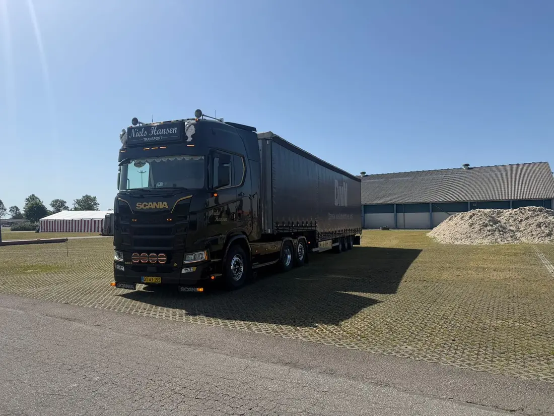 Sort lastbil med sort gardintrailer holder på græsset i skarp sol
