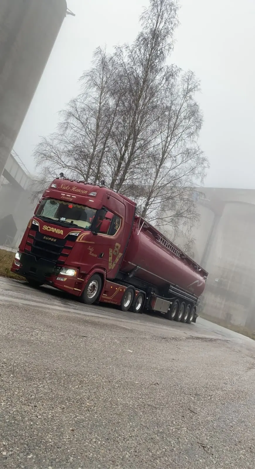 Lastbil med tanktrailer mellem høje siloer i tåge