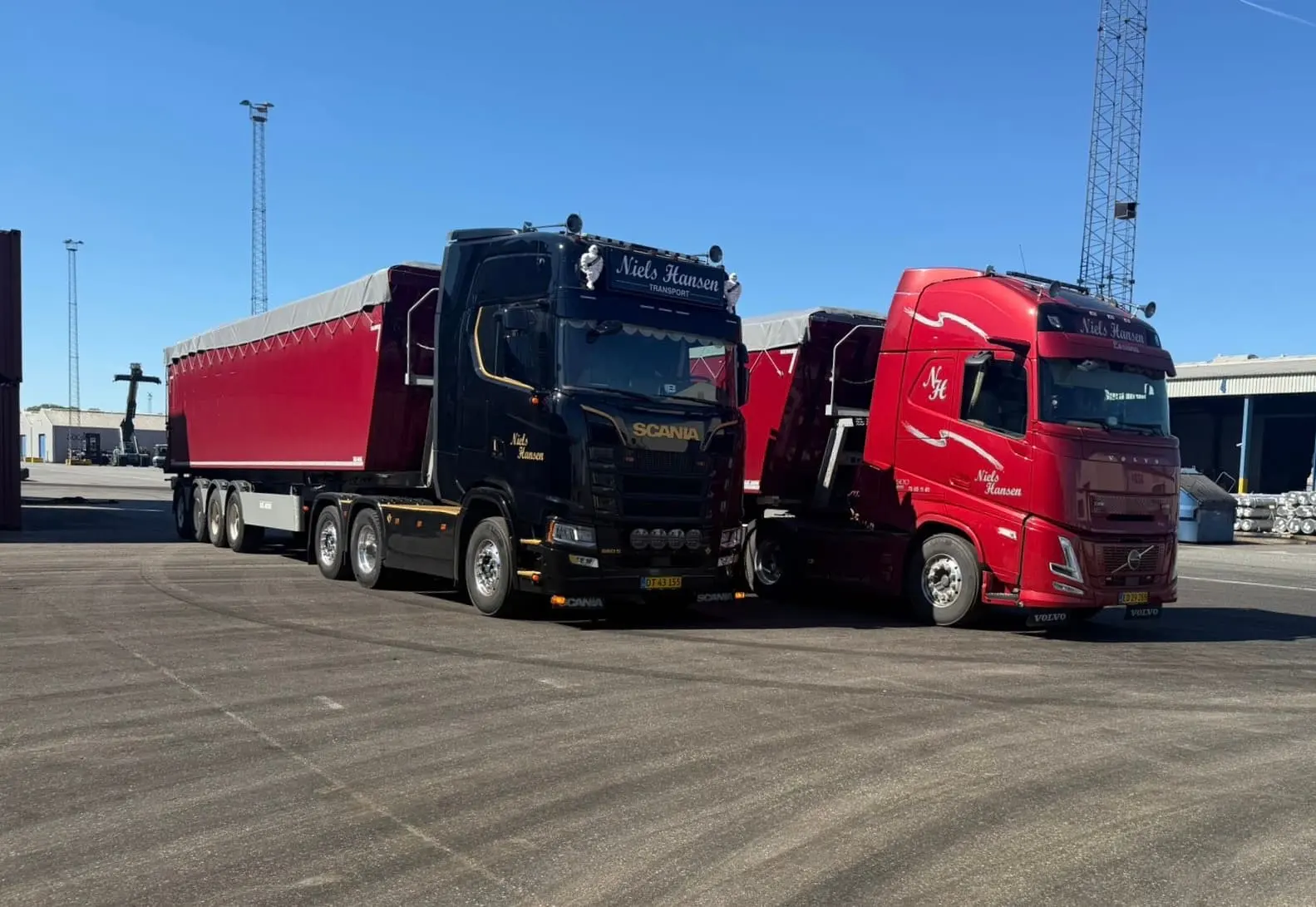 En sort og en rød lastbil holder side om side med tippertrailere i solskin